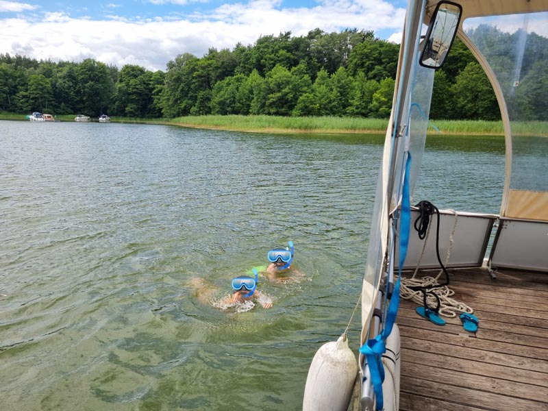 2 Personen schwimmen neben dem Boot, das vor Anker liegt